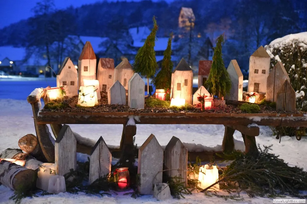 Beleuchtete Holzhäuschen und Kerzen im Schnee vor winterlichem Zainingen